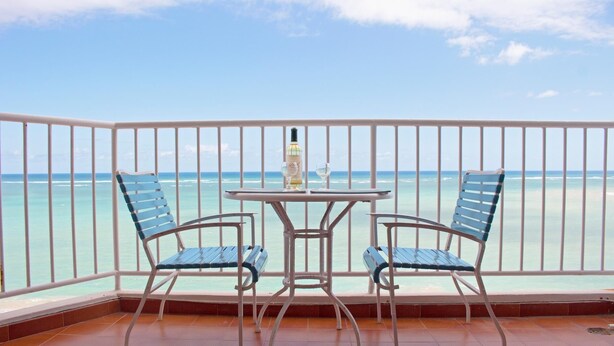 Un balcon avec deux chaises et une table, donnant sur une plage aux eaux turquoise et cristallines.