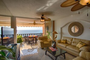 Amplia sala de estar con balcón vista al mar, amueblada con sofá, sillón y mesa de comedor.