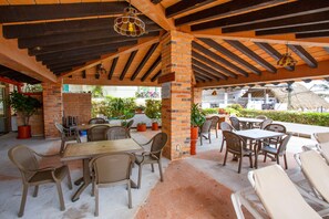 An outdoor patio area with brick pillars, wooden tables, and wicker chairs. - Playa Bonita Casa de los Abuelos located on Los Muertos Beach 2BD Condo for rent (Puerto Vallarta)
