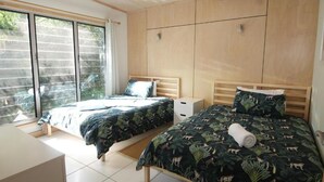 Une chambre avec deux lits, une grande fenêtre et une armoire en bois.
