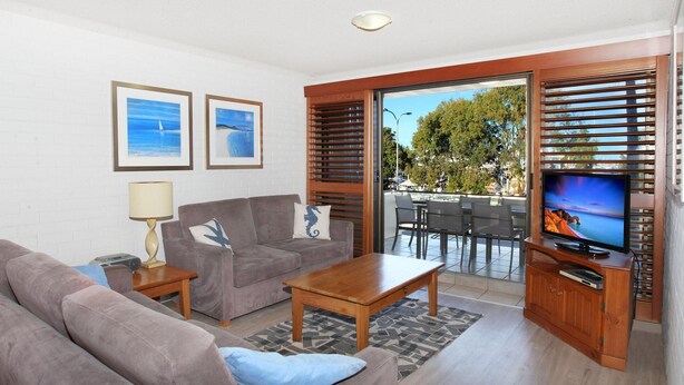 A living room with a sofa, coffee table, TV, and a view of the outdoors.