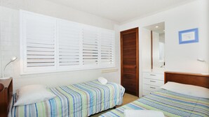 A room with two single beds, a wooden wardrobe, a mirror, and a small desk with a lamp.