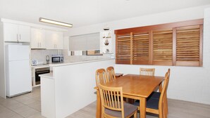 A compact kitchen with white cabinets, a microwave, and a dining area with wooden chairs and a table.