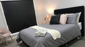 A modern bedroom with a large bed, grey bedding, a white throw blanket, and a pair of rolled towels. - Bacchus Marsh Villa unit 1 (Darley)