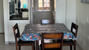 Un coin repas avec une table recouverte d’une nappe ornée de personnages de dessins animés, entourée de chaises en bois.