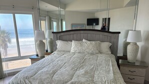 Une chambre avec un grand lit, deux tables de chevet avec des lampes, une télévision et une vue sur la plage.
