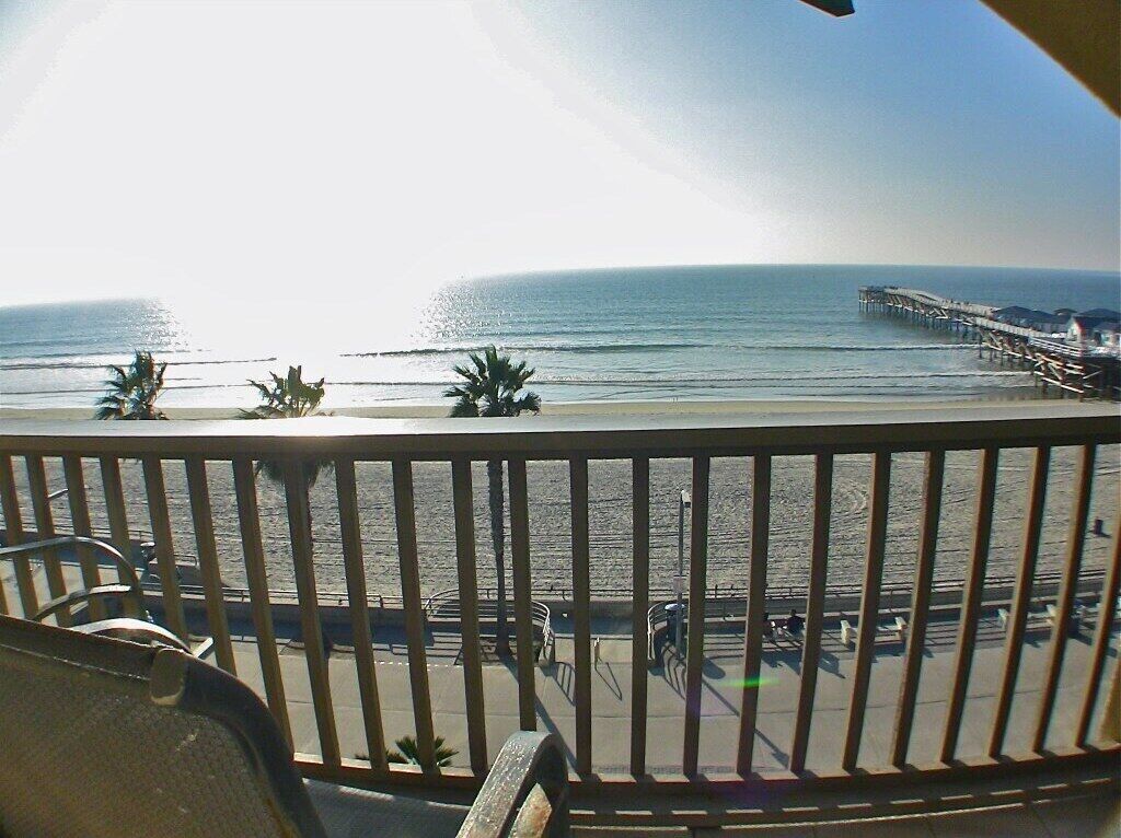 A balcony with a view of the beach, palm trees, and a pier.