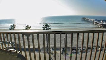 A balcony with a view of the beach, palm trees, and a pier.