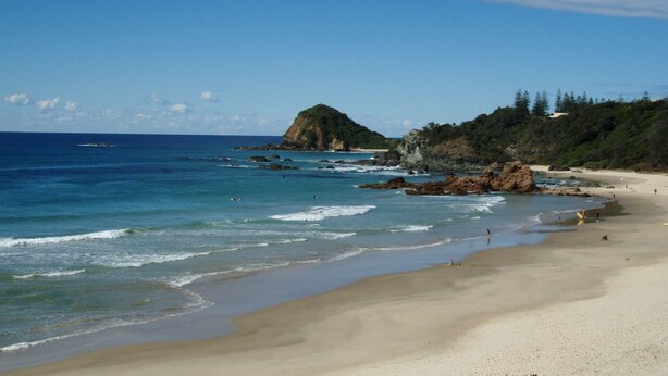 Uma praia com águas azul-claras, areal arenoso e formações rochosas.