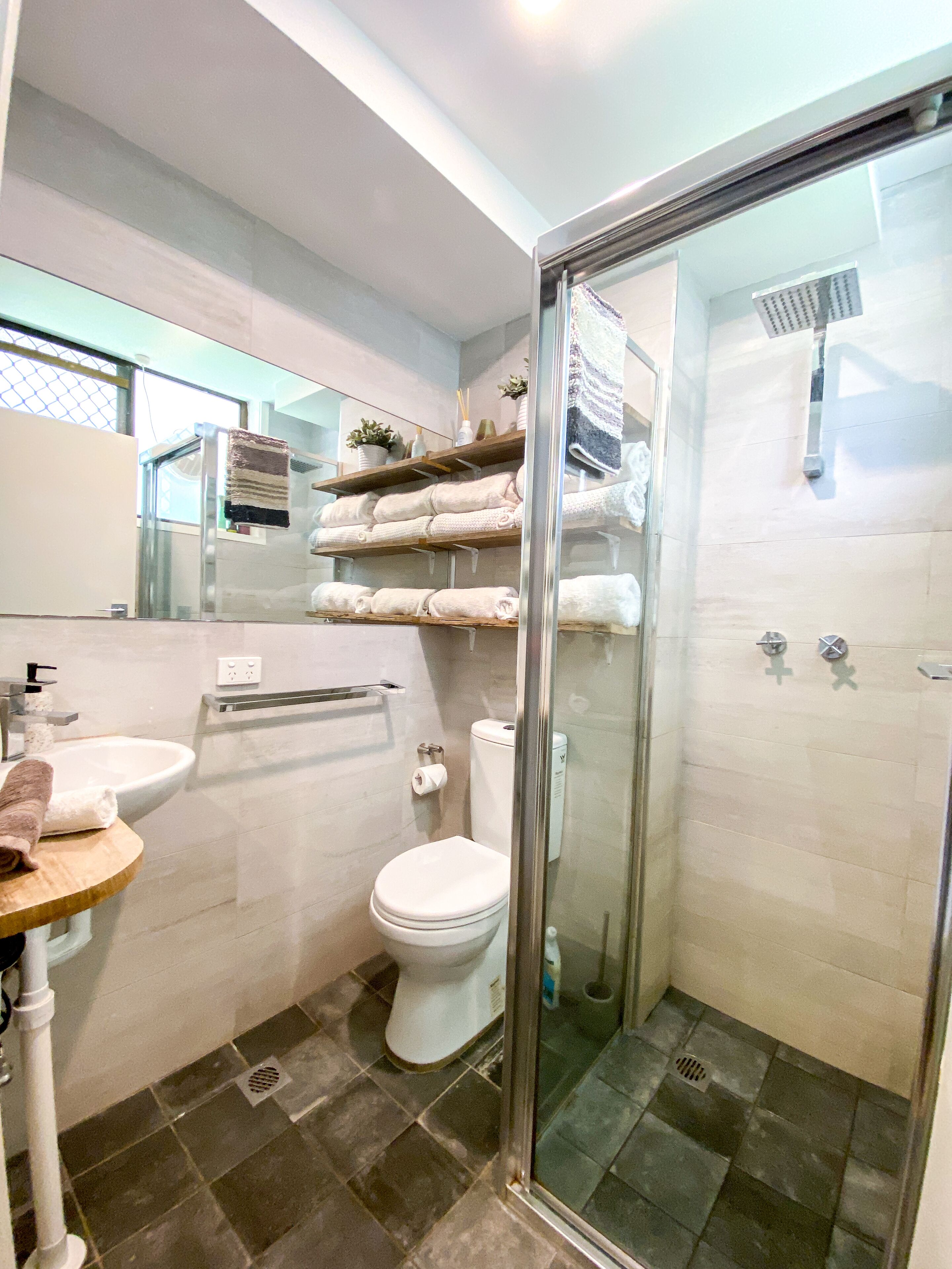 A modern bathroom with a glass shower enclosure, a white toilet, and a sink with a towel rack.