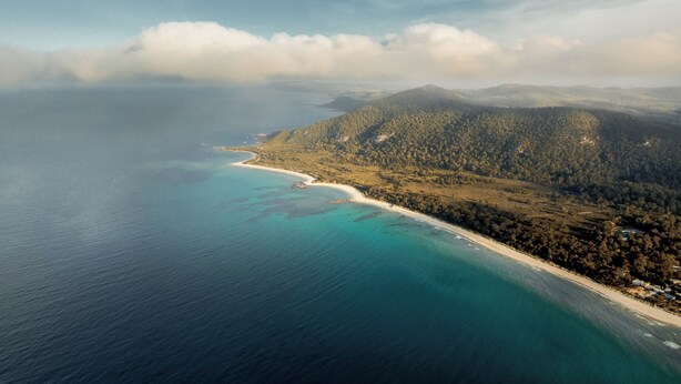 An aerial view of a coastal area with a beach, forested hills, and a clear sky. - Sisters Beach Retreat (sisters beach)
