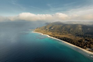 Vista aérea de una zona costera con playa, colinas boscosas y cielo despejado.