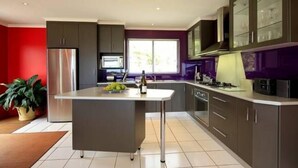 A modern kitchen with a central island, stainless steel appliances, and dark cabinetry. - Sisters Beach Retreat (sisters beach)