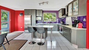 A modern kitchen with a central island, bar stools, and a built-in microwave. - Sisters Beach Retreat (sisters beach)