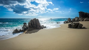 A beach with clear skies, calm sea, and rocky formations. - 2 FREE NIGHTS IN CABO at Casa Alcini! (Cabo San Lucas)