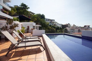 Une piscine sur le toit, agrémentée de chaises longues et entourée de carreaux de terre cuite et de plantes en pot.