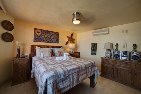 Une chambre à coucher avec un lit, une table de chevet, une commode avec des haut-parleurs et un tableau au mur.