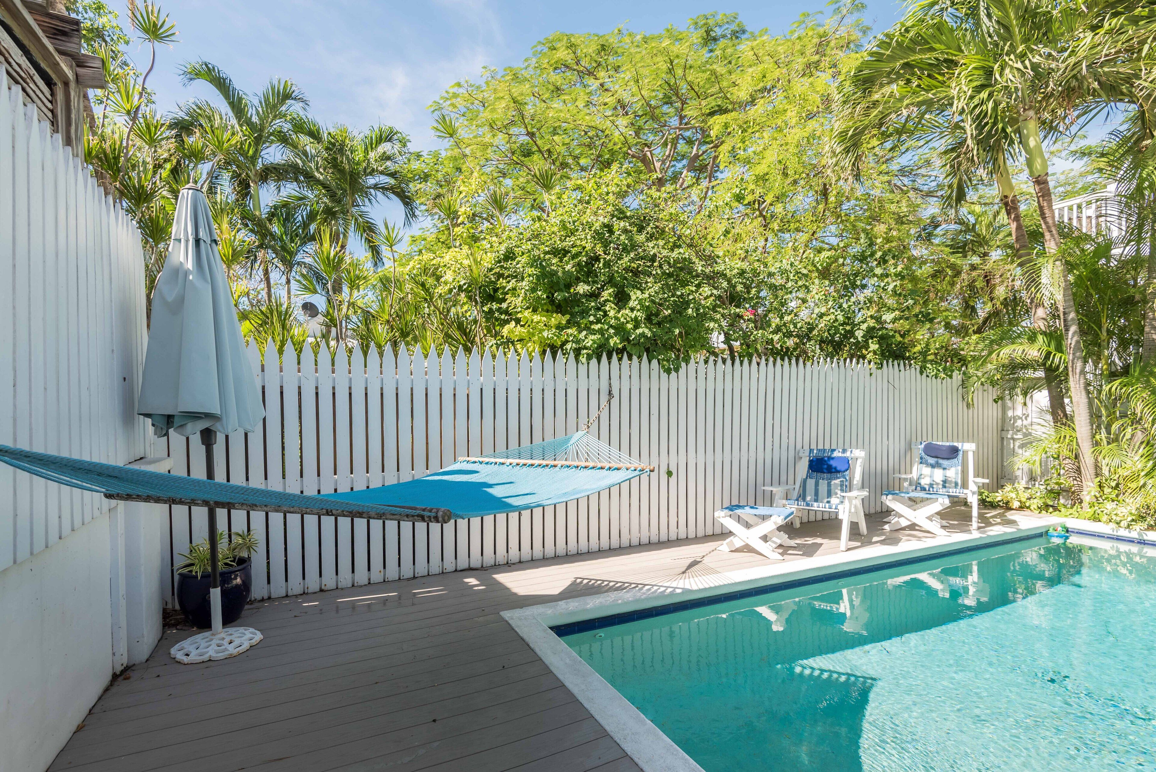 A pool area with a white fence, palm trees, and lounge chairs.