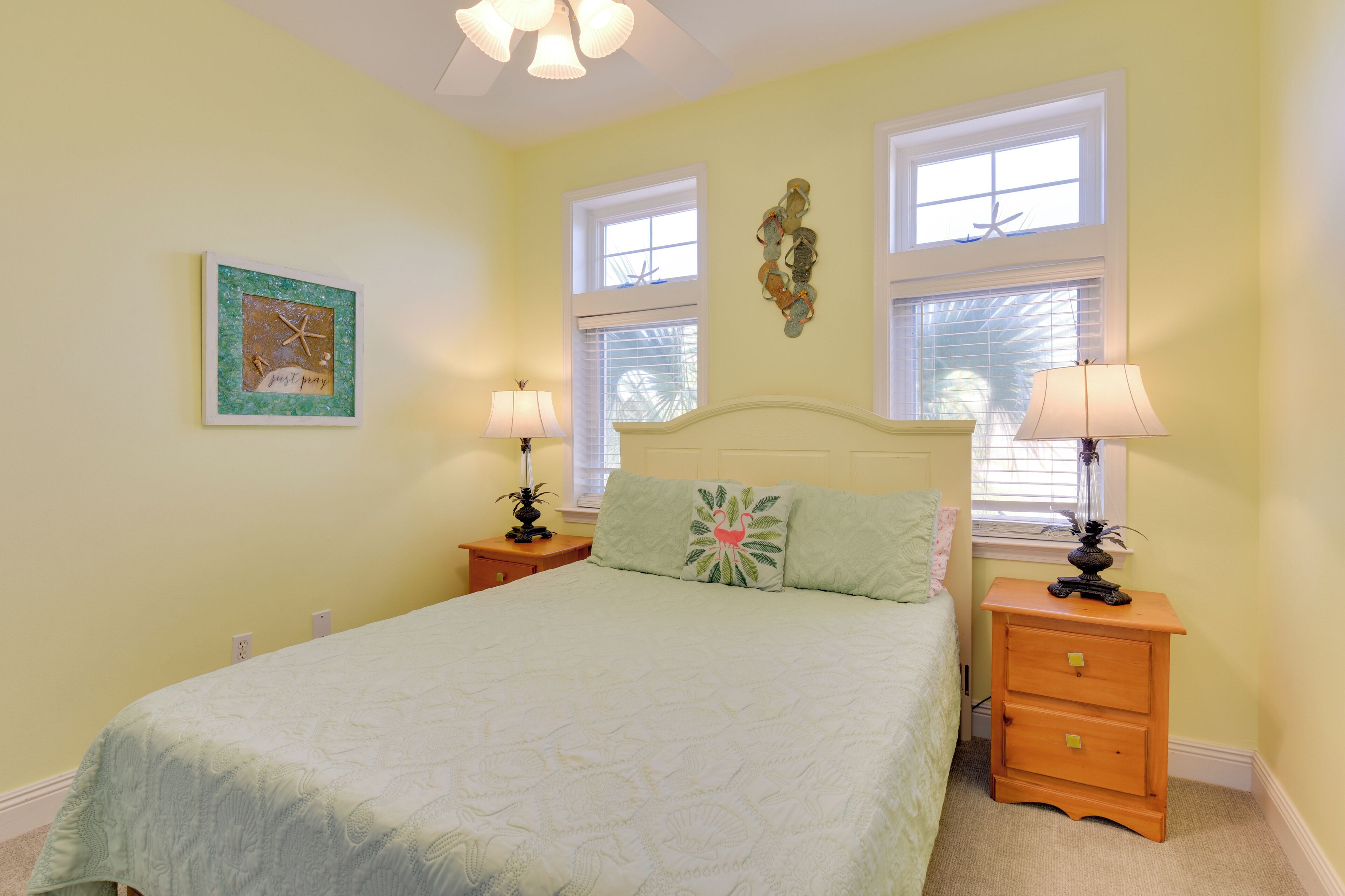 A bedroom with a bed, two nightstands, two lamps, a window with blinds, and a wall decoration.