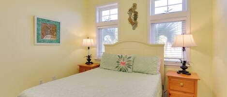 A bedroom with a bed, two nightstands, two lamps, a window with blinds, and a wall decoration.