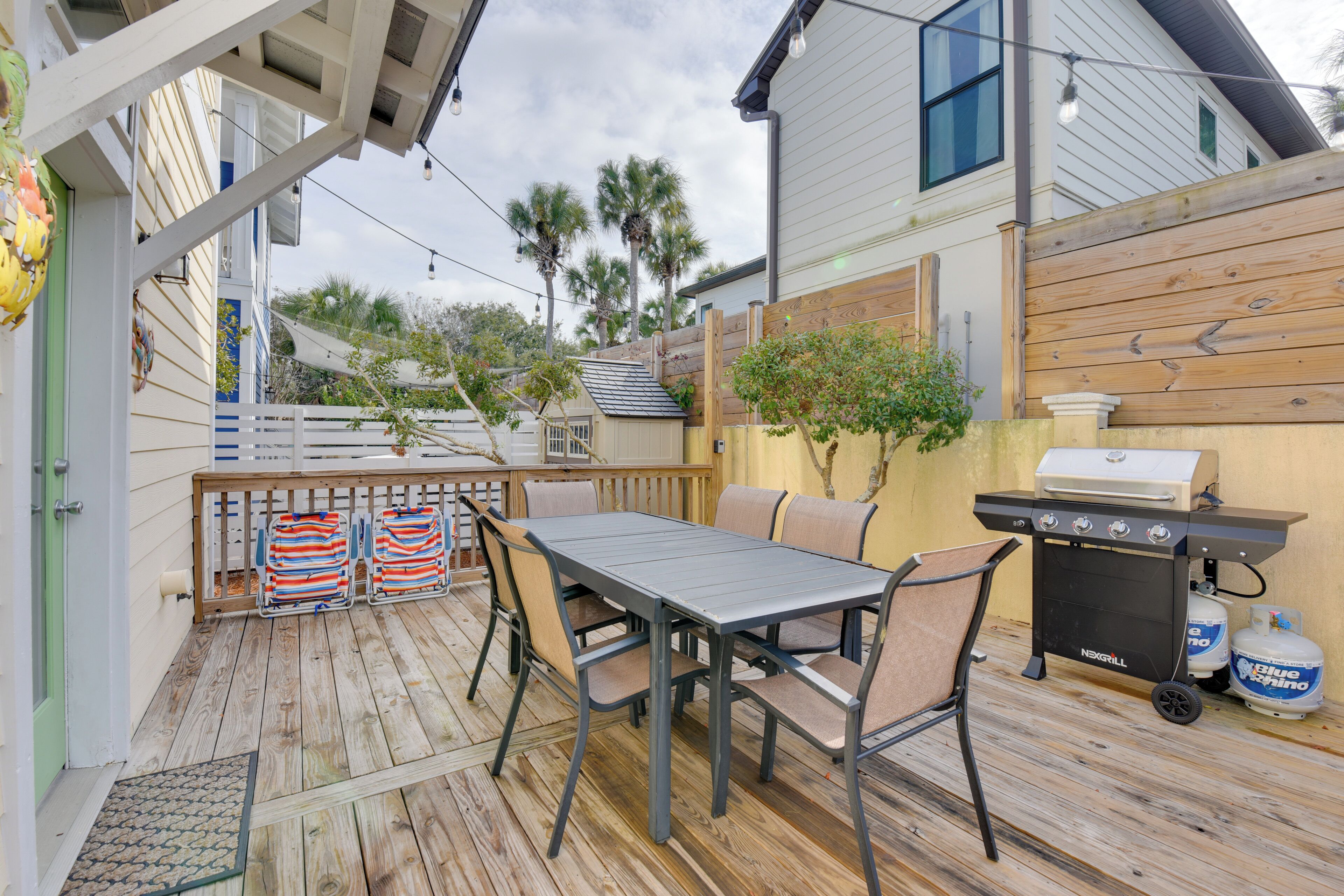 A wooden deck with a table and chairs, a grill, and a white fence.