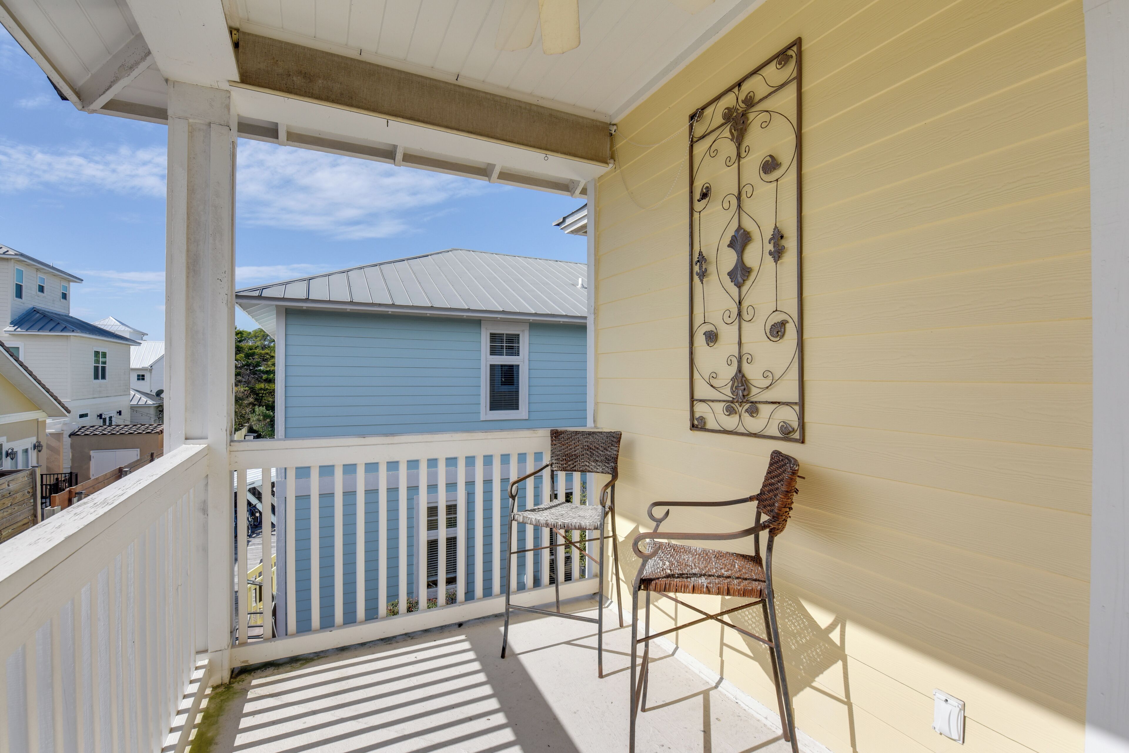 A balcony with a white railing, two wicker chairs, and a decorative metal piece on the wall.