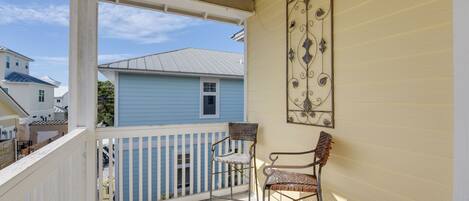 A balcony with a white railing, two wicker chairs, and a decorative metal piece on the wall.