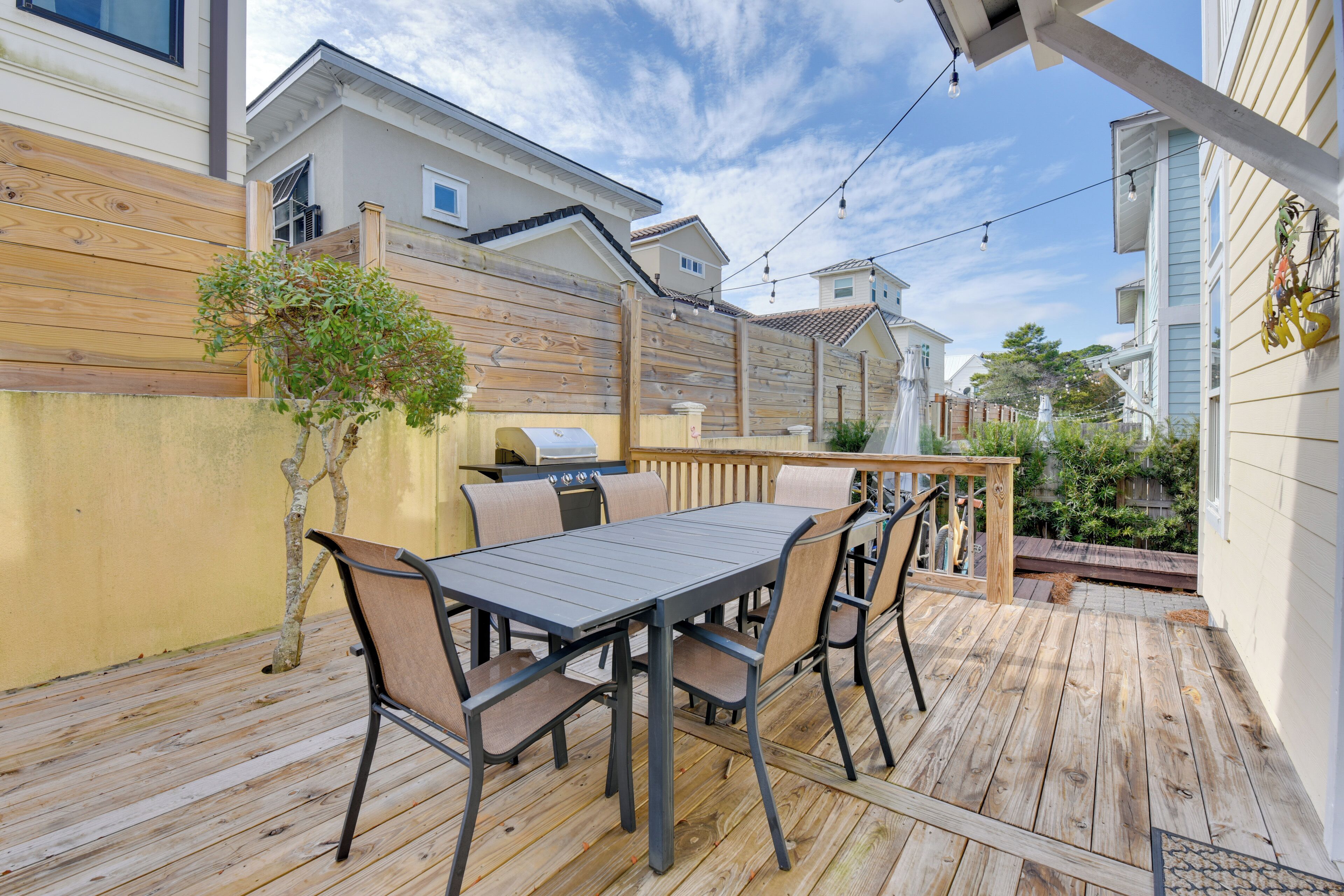 Una terraza de madera con una mesa, sillas, una parrilla y una valla de madera.