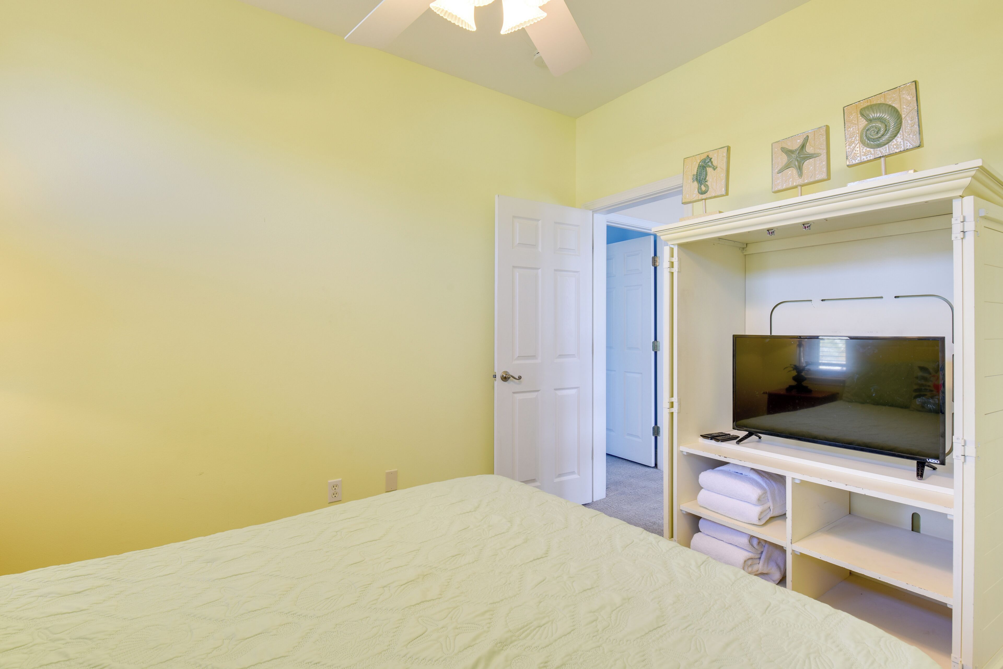 A bedroom with a bed, a TV on a stand, and a door leading to another room.