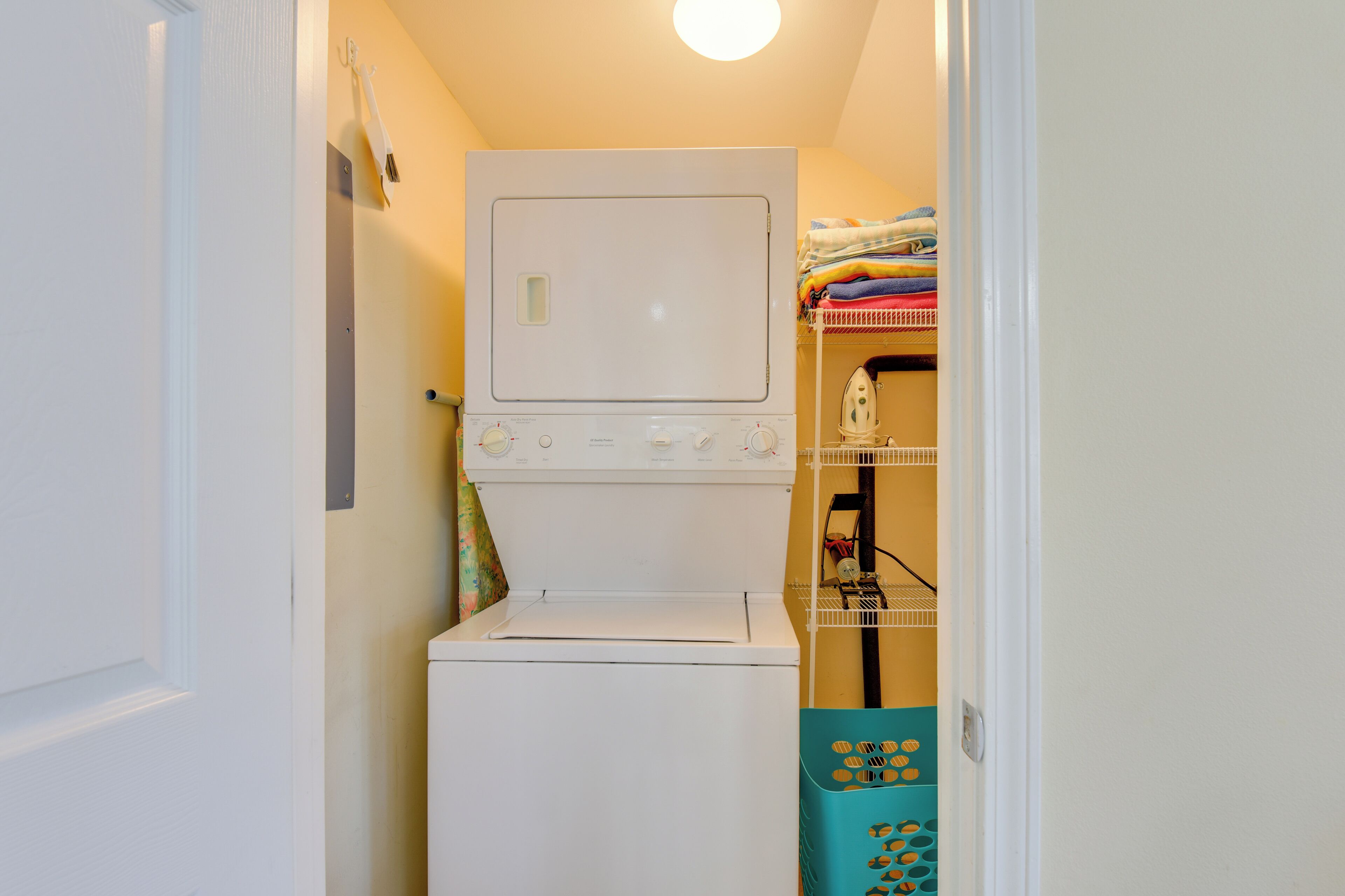 A compact laundry room with a washer and dryer, a drying rack, and a shelf with folded towels.