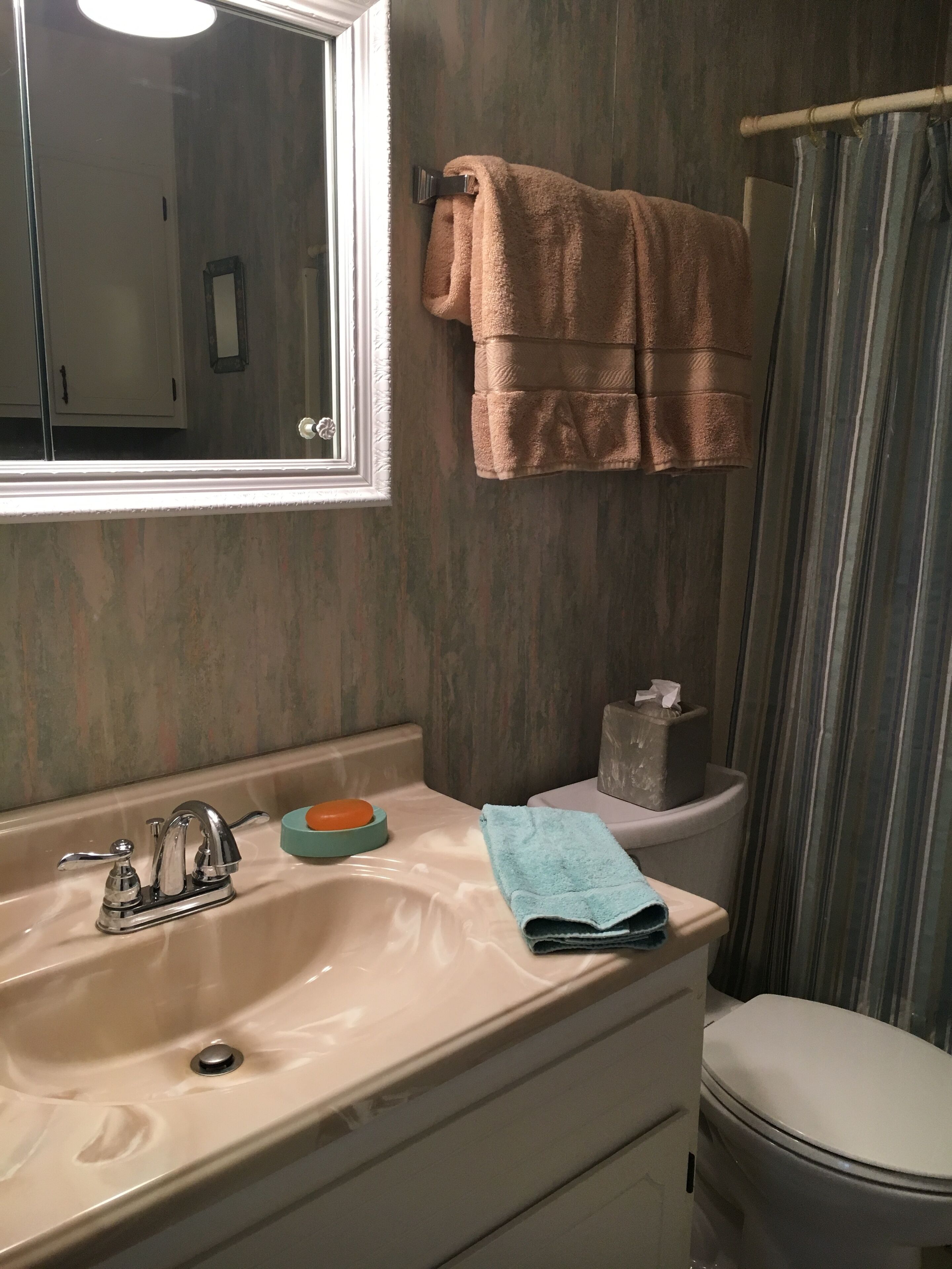 A bathroom with a sink, mirror, towel rack, toilet, and shower curtain.