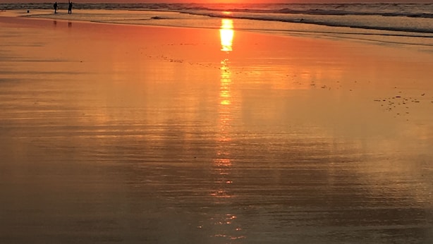 A beach at sunset with the sun reflecting on the wet sand.