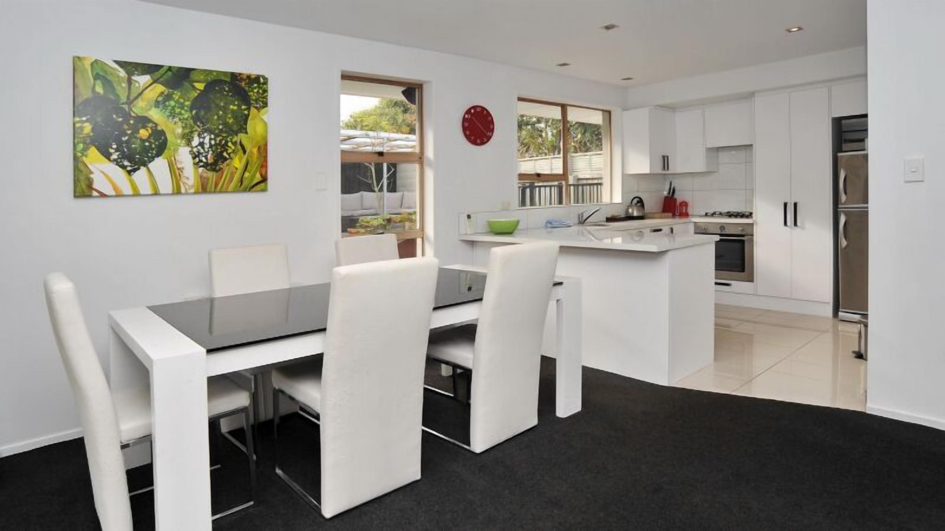 A modern kitchen with white cabinetry, a central island, and a dining area with a black table and white chairs.