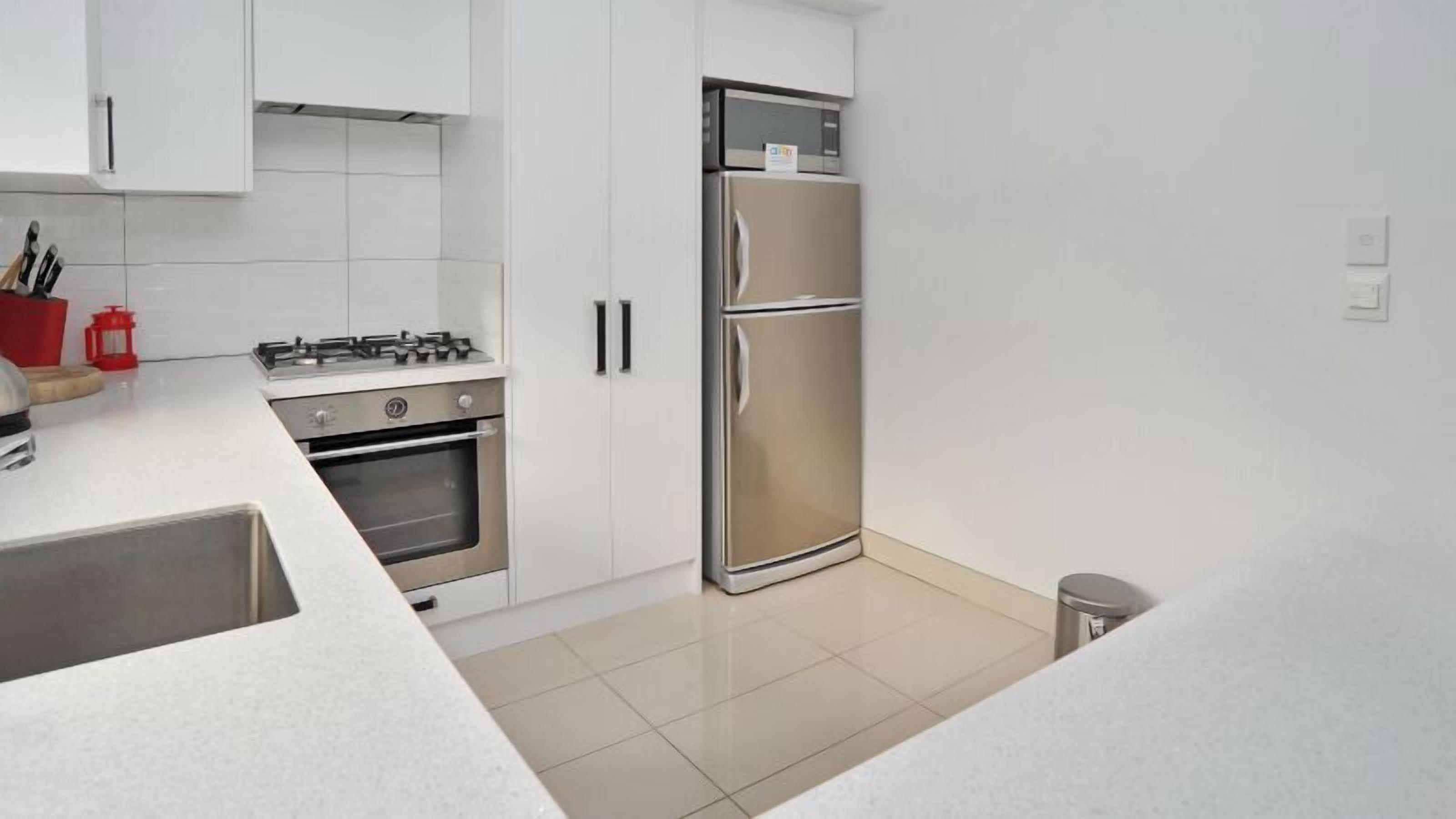 A modern kitchen with white cabinets, a stainless steel refrigerator, a gas stove, and a built-in oven.