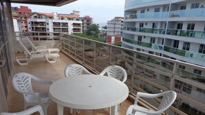 A balcony with a round table and white plastic chairs, overlooking a cityscape with multi-story buildings. - MAKE YOURSELF AT HOME! Spacious, 4 bedrooms, air conditioning, free Wi-Fi, close to the street market! (Cabo Frio)