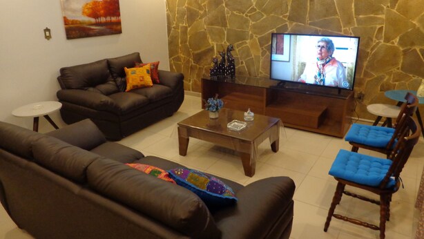 A living room with a stone wall, a brown leather sofa, a coffee table, and a television. - MAKE YOURSELF AT HOME! Spacious, 4 bedrooms, air conditioning, free Wi-Fi, close to the street market! (Cabo Frio)