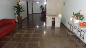 A hotel lobby with a red sofa, a reception desk, potted plants, and a tiled floor. - MAKE YOURSELF AT HOME! Spacious, 4 bedrooms, air conditioning, free Wi-Fi, close to the street market! (Cabo Frio)