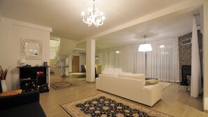 Ein geräumiges Wohnzimmer mit einem weißen Sofa, einem großen Teppich in Schwarz und Gold sowie einem Kronleuchter.