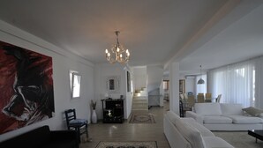 Ein geräumiges Wohnzimmer mit einem großen Gemälde, einer Chandelier und einer Treppe, die zu einer anderen Ebene führt.