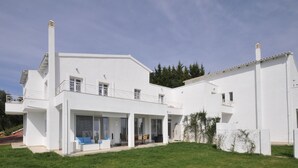 Ein modernes, weißes, zweistöckiges Haus mit überdachter Terrasse und separater Garage.