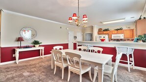 A dining area with a white table and chairs, a chandelier, and a red and white color scheme. - 1021 Willow Bend - Barefoot Resort Rentals (North Myrtle Beach)