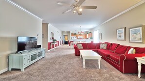 A living room with a red sofa, a TV, and a ceiling fan. - 1021 Willow Bend - Barefoot Resort Rentals (North Myrtle Beach)