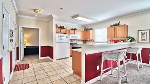 A compact kitchen with a central island, wooden cabinets, a refrigerator, and a microwave. - 1021 Willow Bend - Barefoot Resort Rentals (North Myrtle Beach)