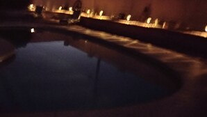Un área de piscina tenuemente iluminada, con reflejos de luces en la superficie del agua.