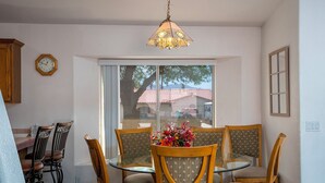Un comedor con mesa de vidrio y sillas de madera, una lámpara colgante y una ventana con vista a un edificio de techos rojos.