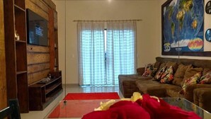 Sala de estar com parede de madeira, um sofá, um tapete vermelho e uma televisão na parede.