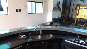 Cozinha com bancada preta, pia e fogão. Há uma janela sobre a pia e uma porta à esquerda.