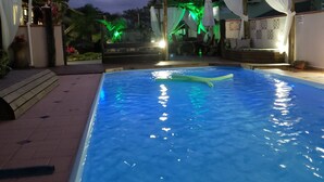 Piscina com superfície de água azul cristalina, rodeada por um terraço com pérgola e mobiliário de exterior.
