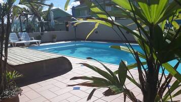 Piscina com deck revestido, rodeada por plantas em vasos e algumas cadeiras de descanso.