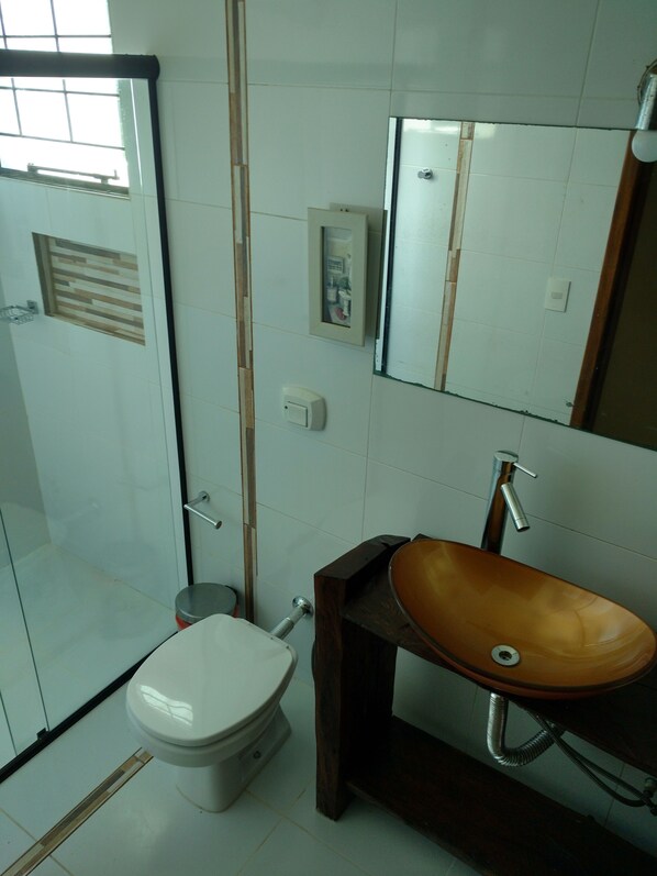 A bathroom with a toilet, a wooden sink, a mirror, and a shower area.